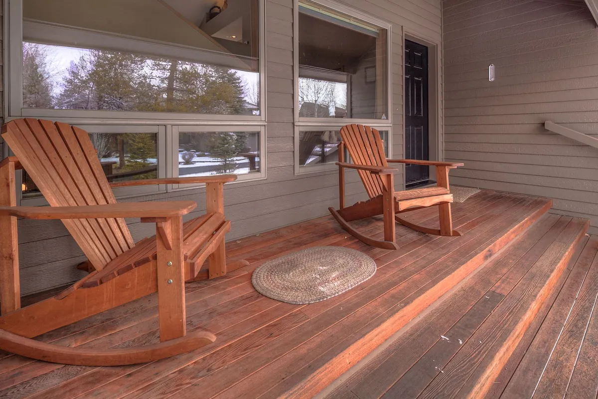 A cozy front porch featuring rocking chairs and a decorative rug, set against a backdrop of trees. The space welcomes guests and pets alike, offering an inviting spot to enjoy early mornings or evening sunsets.