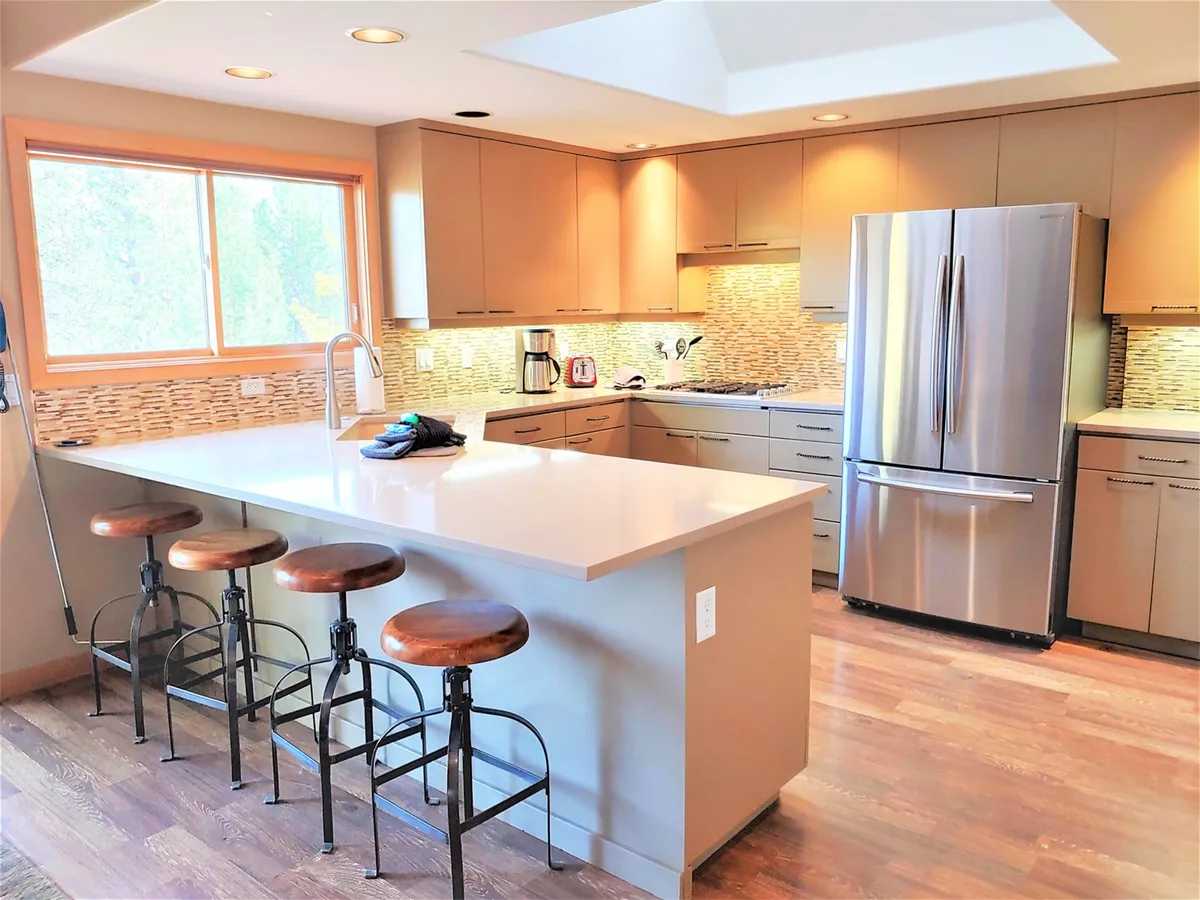 A welcoming view of the kitchen featuring a large island with stools, a window that fills the area with natural light, sleek cabinetry, and prominent stainless steel appliances. The island and open layout invite both meal preparation and social interaction.