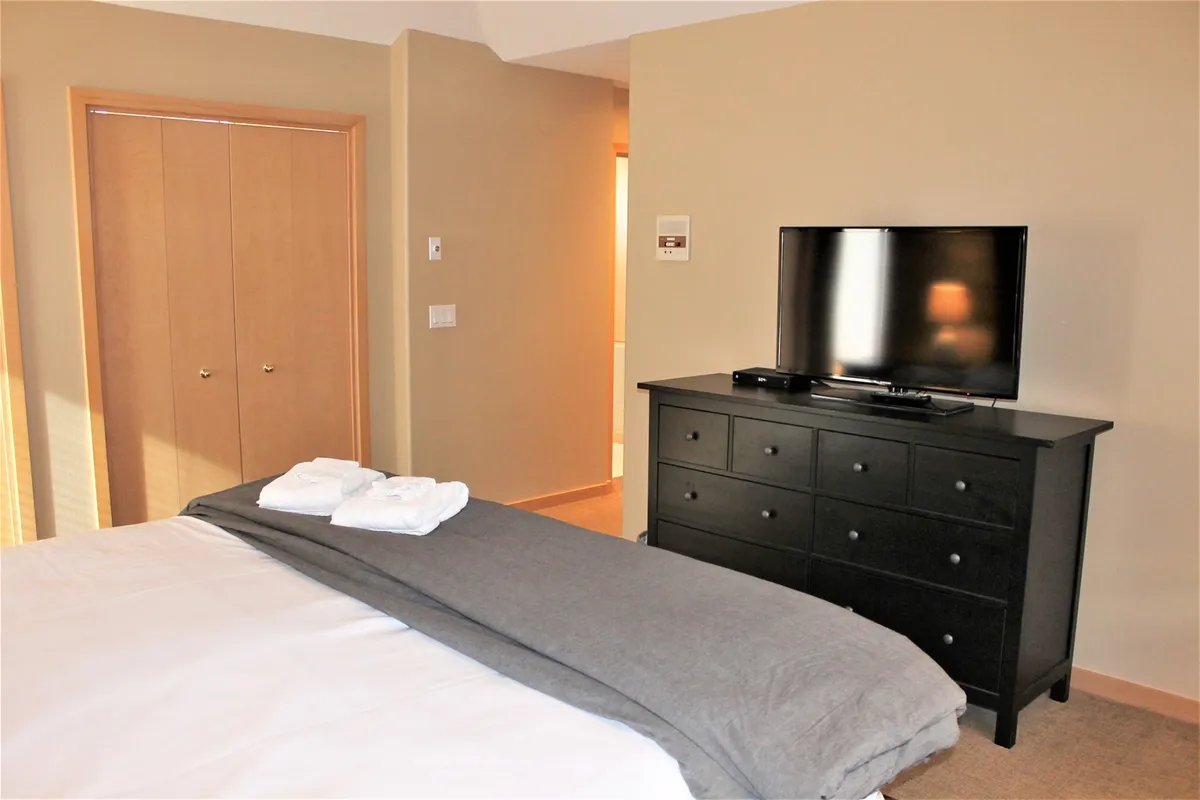 A tastefully decorated bedroom with a plush bed, flat-screen television, and a practical dresser. The space is styled for comfort, inviting guests to relax, unpack, and feel at home.