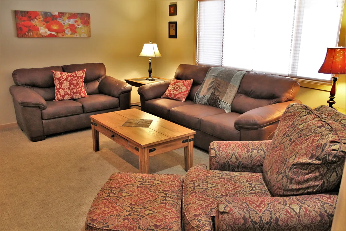 An intimate living area with brown leather sofas, a wooden coffee table, decorative cushions, table lamp, and wall art. The space feels inviting—ideal for reading, socializing, or unwinding in comfort.