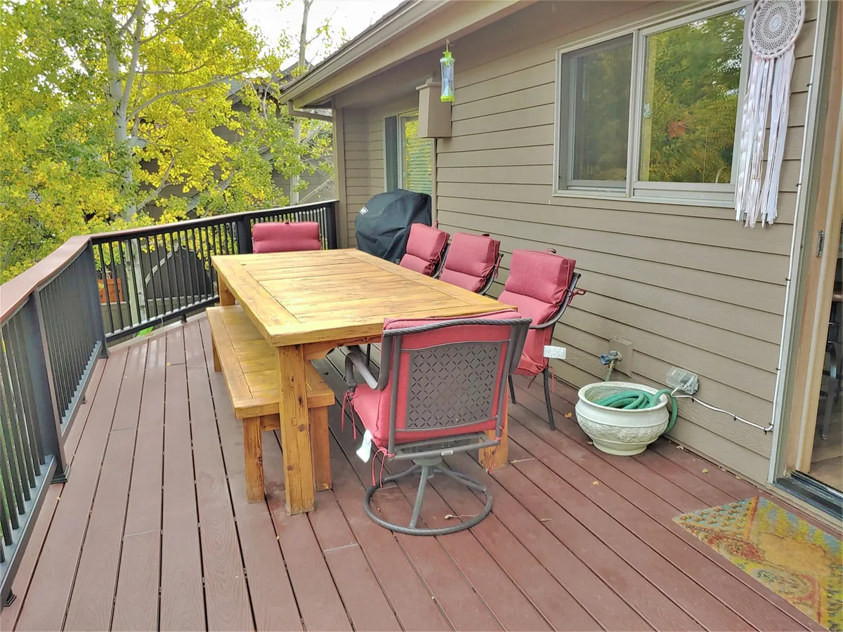 An exterior view showcasing a wooden table surrounded by red cushioned chairs, framed by lush green plants. The space is set up for outdoor dining, gatherings, and barbecues, with ample room to relax and socialize. The natural surroundings create an inviting atmosphere for post-adventure relaxation or group activities.