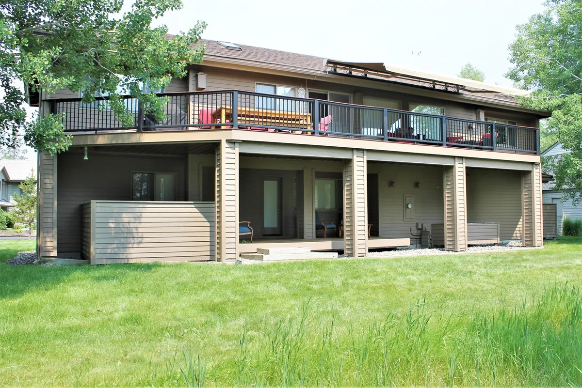 A wide shot highlighting an upper balcony with seating, a ground-level patio, and a lush green lawn—ideal for outdoor relaxation or post-adventure downtime. The layered outdoor spaces offer visual cues for gathering together or enjoying solo moments, with a backdrop of greenery to suggest connection with Sunriver's natural setting.