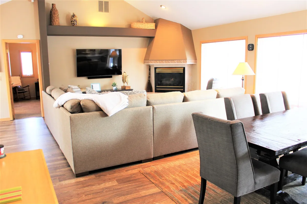 A welcoming interior scene showcases a cozy living area with a plush sofa, a fireplace, a dining table, and a television. The space is designed for relaxing, entertaining, or enjoying quiet evenings after a day of adventure.
