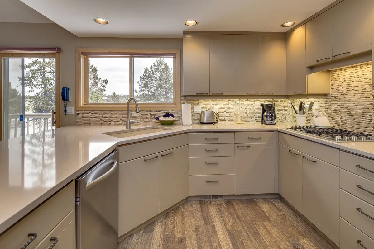 A modern kitchen scene showcasing a generous island, a bright window, and an array of top-notch appliances including a stylish refrigerator and textured backsplash. The setup is clearly designed for both cooking and entertaining guests.