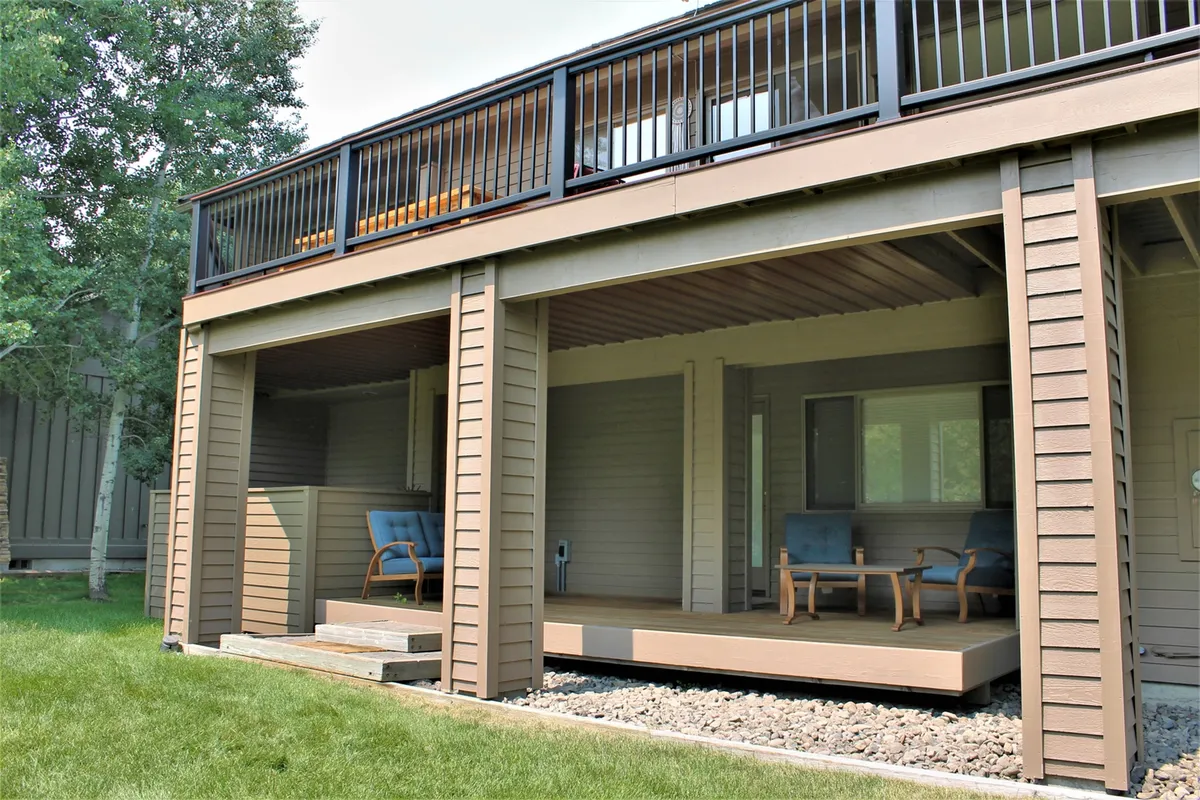 A tranquil backyard deck with patio chairs overlooking a landscaped grassy area, bordered by lush trees. The setting offers a comfortable spot to relax, socialize, or enjoy the peaceful outdoors after a day on the trails.