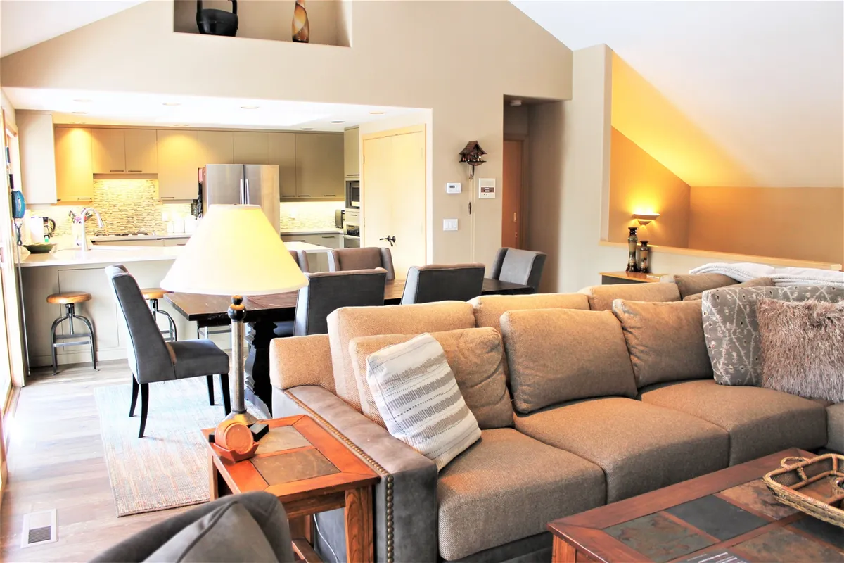 A unified living and dining space with a large sectional sofa, a prominent dining table, and a visible kitchen area in the background. The layout is cozy yet open, ideal for both casual family meals and festive gatherings.