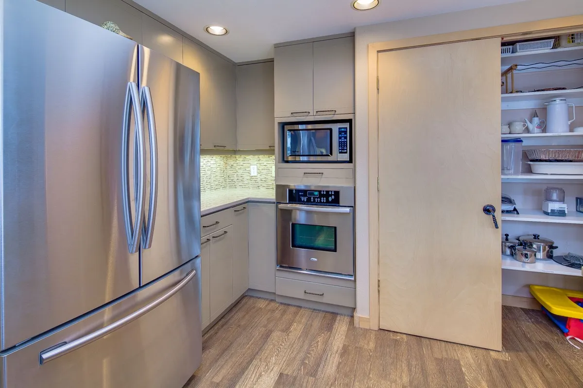 A modern kitchen scene with a stainless steel refrigerator, built-in oven and microwave, and a pantry door. The space is designed for cooking, meal preparation, and entertaining, with a contemporary and inviting atmosphere.